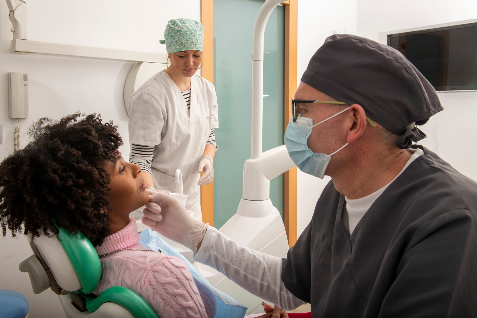 Dentist examining patient's teeth in dental clinic with assistant preparing tools