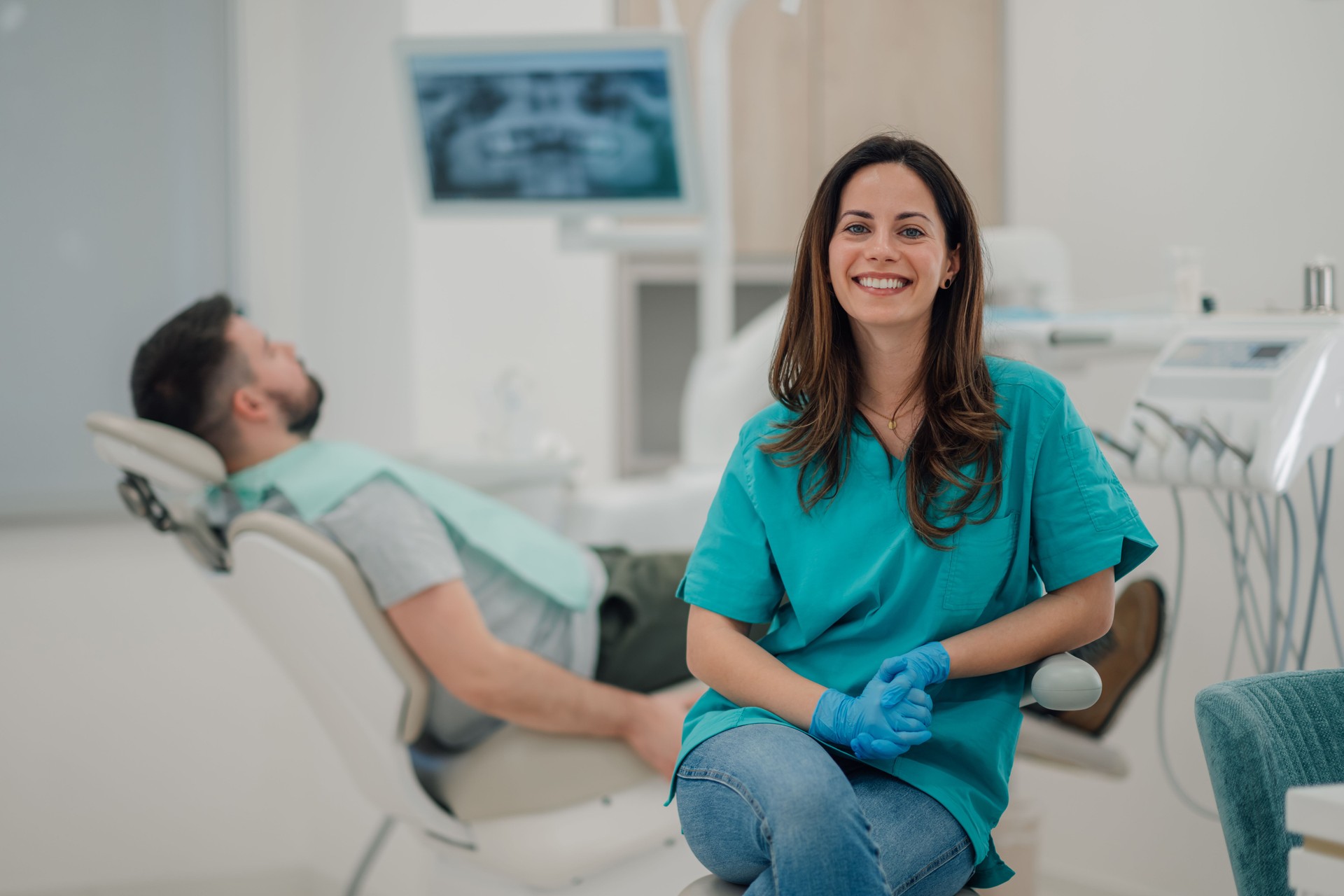 Dentist smiling at the dental office with patient on background